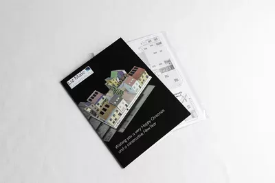 A black architectural portfolio or brochure featuring interior design renderings of a residential space, placed on top of white architectural floor plans and sketches on a light gray background.