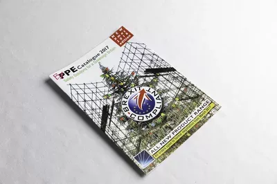 A printed magazine or publication lies at an angle on a white surface, with a geometric net pattern overlay and a circular logo visible on its cover, alongside green mesh netting material.