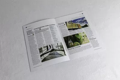 An open magazine or brochure spread displaying articles with multiple photographs including architectural and nature imagery, laid flat on a white surface at an angle.