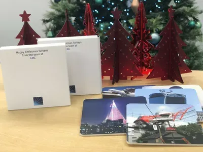 Holiday greeting cards and printed photos arranged on a wooden surface, with burgundy decorative tree ornaments and evergreen garland in the background.