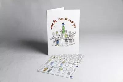 A folded white greeting card with an illustration of a family decorating a Christmas tree and red text reading 