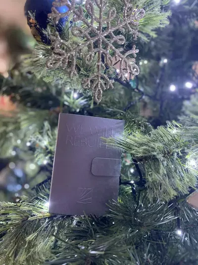 A small purple wallet with a square button detail nestled among evergreen branches and white string lights on a Christmas tree.