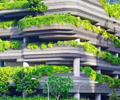 Modern spiral parking garage with abundant green vegetation and climbing plants covering the curved concrete levels, demonstrating sustainable urban design and integration of nature into built infrastructure.