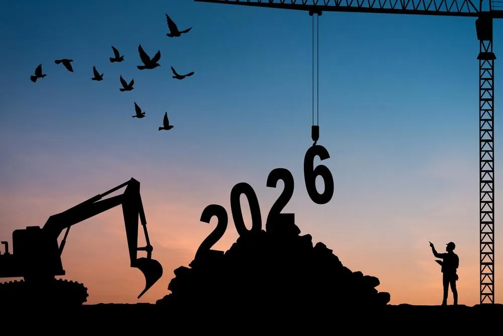 A silhouette of construction equipment and workers building the year 2026, set against a sunset sky with birds flying overhead, symbolizing future development and growth in the construction industry.