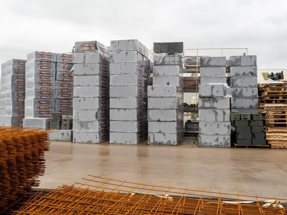 Stacked concrete blocks and wooden pallets on a wet construction site floor under a cloudy sky, representing building materials and construction materials storage.
