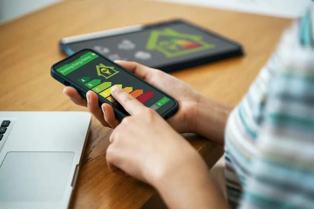 A person holds a smartphone displaying a green and yellow radiation hazard symbol with colored bars, while a tablet with similar content sits blurred in the background on a wooden desk.
