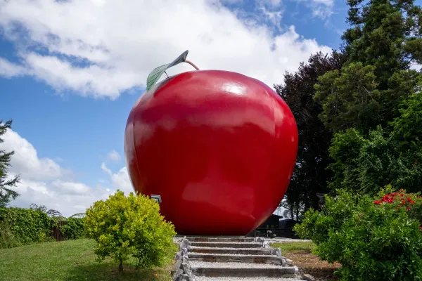 Giant red apple sculpture surrounded by trees and gardens.