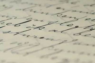 Handwritten cursive script on cream-colored paper with ink pen, showcasing flowing penmanship in varying shades of gray and black.
