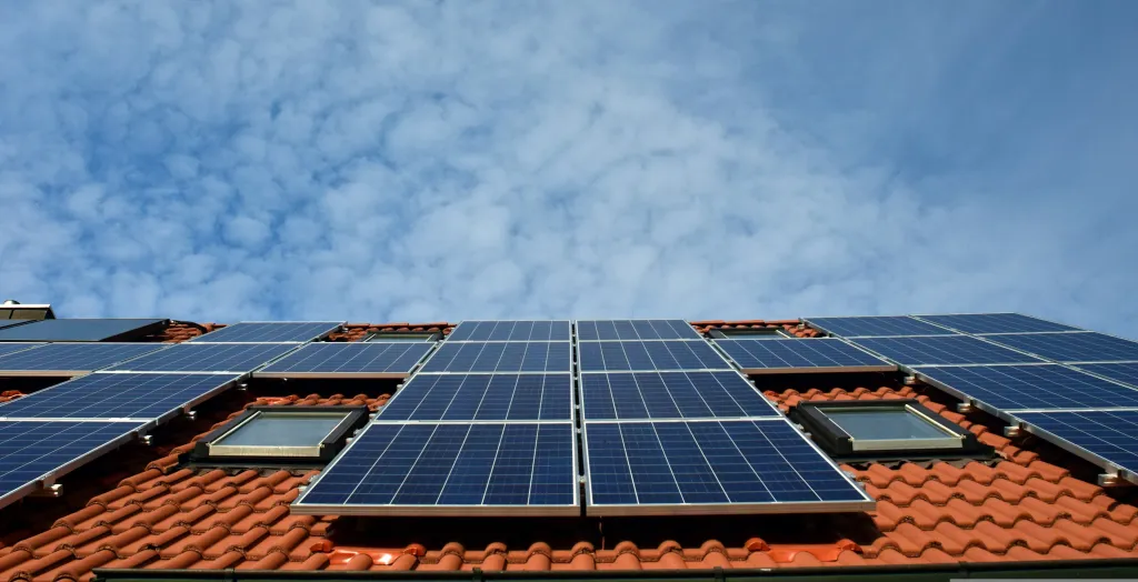 Solar panels installed on an orange tile roof against a blue sky with white clouds.