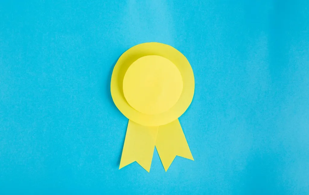 A yellow award ribbon medal with two trailing ribbons against a turquoise blue background.
