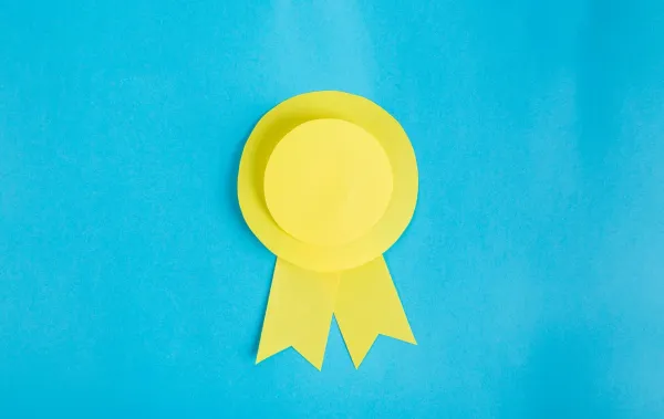 A yellow award ribbon medal with two trailing ribbons against a turquoise blue background.