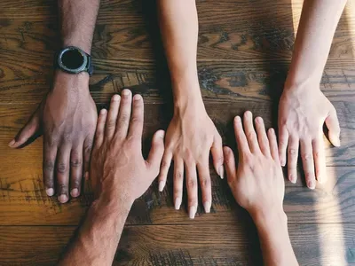 Four people place their hands together in a circle on a wooden table, demonstrating unity and collaboration in community building.