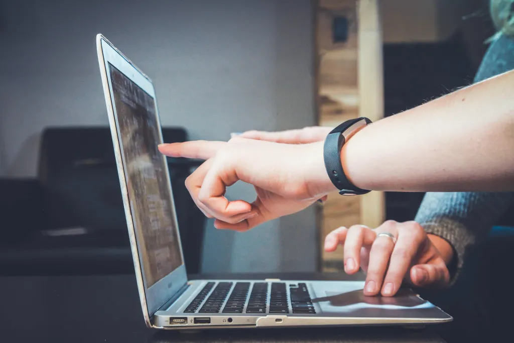 A person wearing a smartwatch points at a laptop screen with both hands engaged, suggesting interaction or demonstration during a live streaming or digital content session.