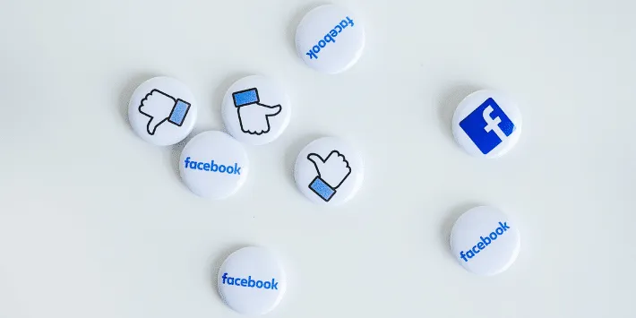 Several white and blue circular tokens scattered on a light background, each displaying the Facebook logo, thumbs-up icon, or the word 