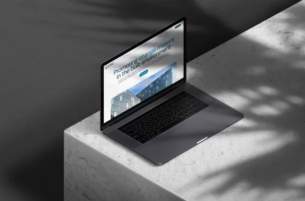 A laptop displaying a webpage for Liz Male Consulting's new lower-carbon digital services, positioned on a concrete surface with dramatic shadows cast across it.