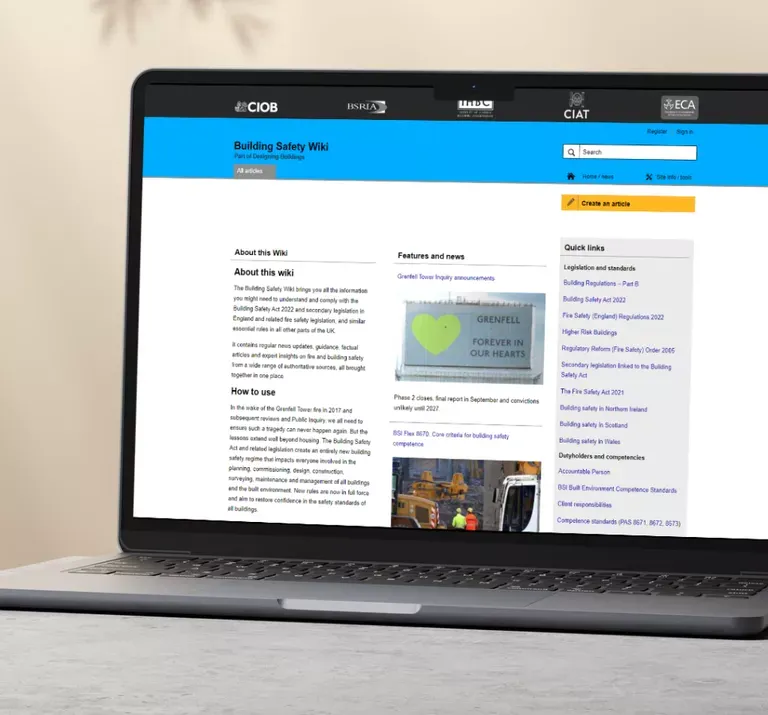 Laptop displaying the Building Safety Wiki homepage from Liz Male Consulting, with blue header navigation, main content sections including 