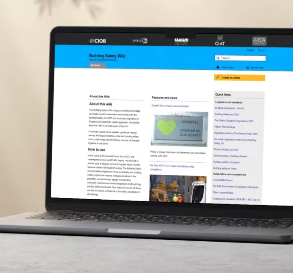 Laptop displaying the Building Safety Wiki homepage from Liz Male Consulting, with blue header navigation, main content sections including 