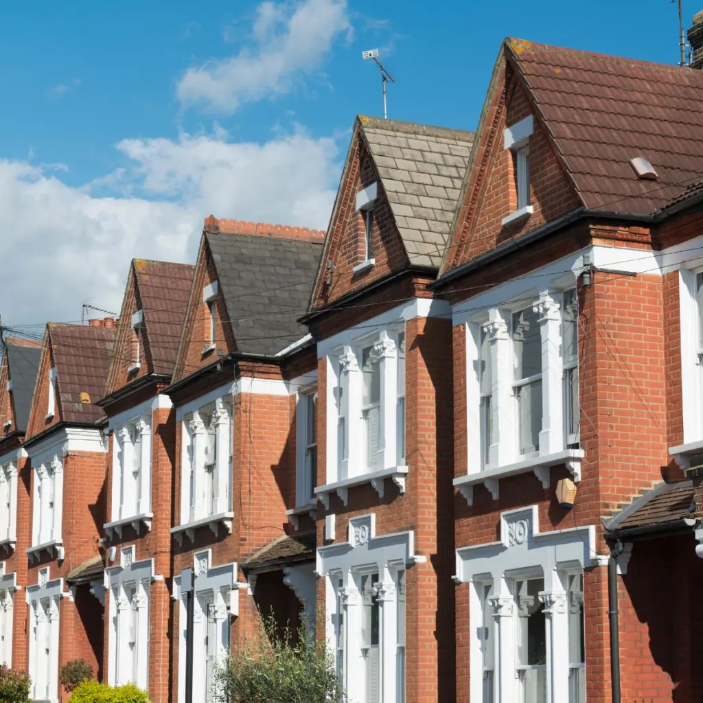 A row of Victorian-era brick townhouses with distinctive gabled roofs, white bay windows, and terracotta tile details typical of British residential architecture.