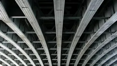 Underside of a concrete bridge or elevated highway structure displaying parallel beams and systematic support columns in black and white.