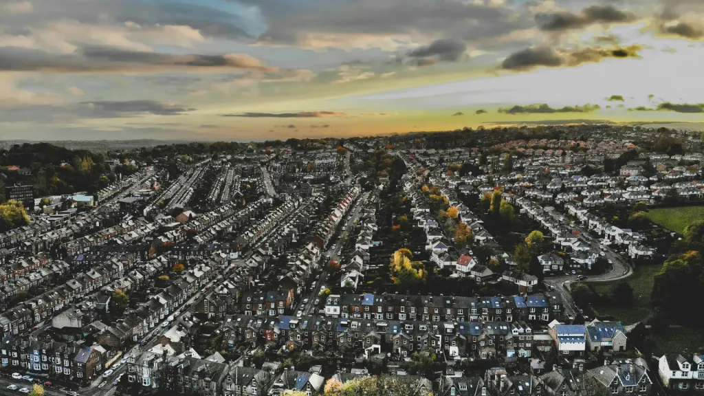 Aerial view of a sprawling suburban neighborhood with rows of residential houses, streets, and green spaces under a partly cloudy sky at sunset or sunrise.