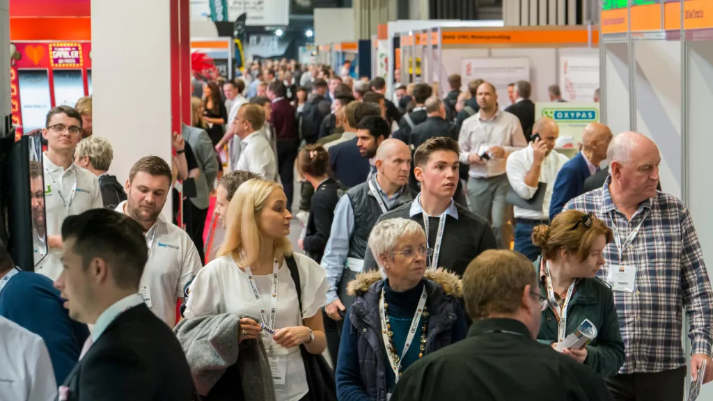 A crowded indoor venue filled with professionals wearing lanyards and badges, many engaged in conversation at what appears to be a networking or conference event related to the built environment industry.