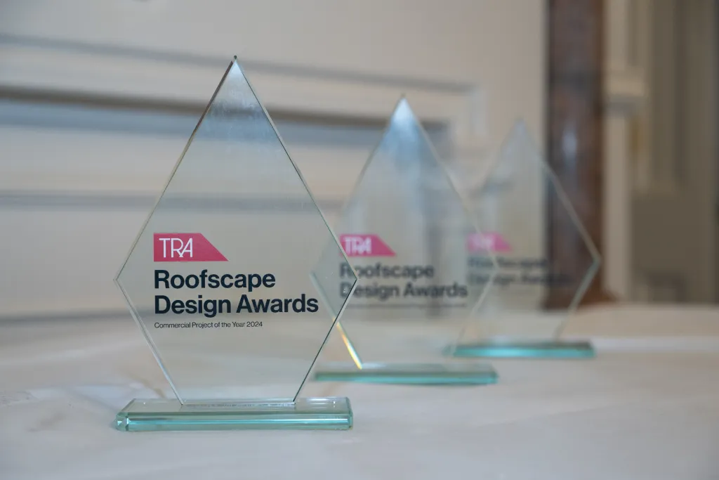 Three clear glass pyramid-shaped trophies with teal bases sit on a white surface, each displaying the TRA Roofscape Design Awards logo with pink and black text. The trophies are arranged in a row with the nearest one in sharp focus while the others blur into the background.