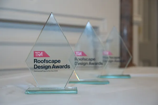 Three clear glass pyramid-shaped trophies with teal bases sit on a white surface, each displaying the TRA Roofscape Design Awards logo with pink and black text. The trophies are arranged in a row with the nearest one in sharp focus while the others blur into the background.